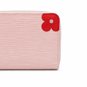 A close-up of a light pink textured leather wallet corner featuring a red flower-shaped leather tab with a silver metal center stud.