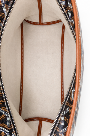 Close-up of the interior of a Goyard bag, showing a beige suede-like lining, brown leather trim, and the brand's signature patterned canvas exterior.