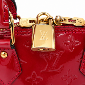 Close-up of a red Louis Vuitton monogram handbag with gold-tone hardware, featuring a padlock closure and embossed floral motifs on a white background.