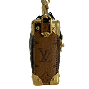 A Louis Vuitton miniature luggage charm in brown monogram canvas with gold-tone hardware and studs, shown standing upright on a white surface.