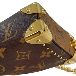 Close-up of a Louis Vuitton monogram handbag corner with gold-tone metal hardware and studs, held by a hand against a light background.