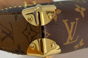 Close-up of a Louis Vuitton handbag in brown monogram canvas with gold-tone hardware and a gold chain strap, held against a light background.