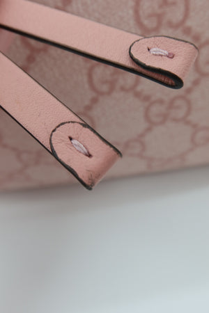 Close-up detail of a light pink leather strap with black edging and a matching pink monogram patterned background.