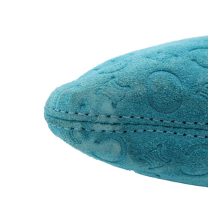 A close-up of a teal blue suede or velvet cushion corner with decorative embossed circular patterns and dark contrast stitching, set against a clean light gray background.