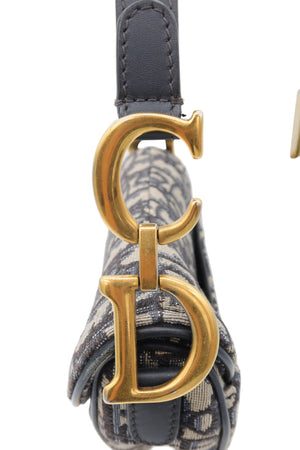 Close-up of a Dior shoulder bag featuring the signature Dior Oblique canvas, dark gray leather strap, and large interlocking gold-tone 'CD' hardware.
