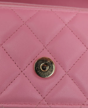 A close-up of a pink quilted leather clutch or wallet featuring a gold-tone circular snap button engraved with the brand name CHANEL.