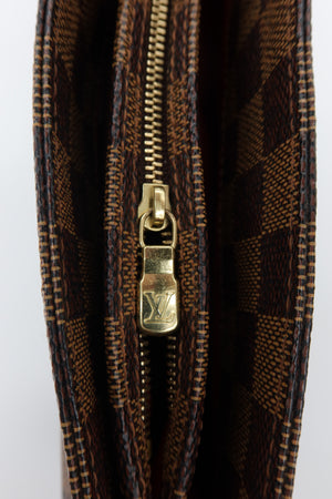 Close-up of a Louis Vuitton monogram canvas zipper, showing the classic brown and black check pattern with a gold-tone metal zipper pull engraved with the LV logo.
