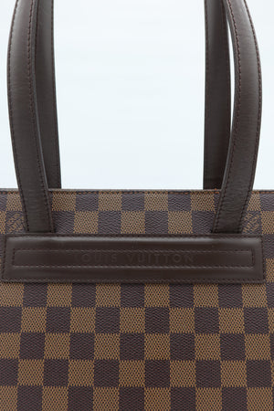 Close-up of a Louis Vuitton handbag in the Damier Ebene checkered canvas with dark brown leather handles and a branded leather tab.