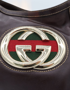 Close-up of a dark brown leather handbag featuring a large polished silver-tone interlocking G logo over the signature green and red web stripe on the front.