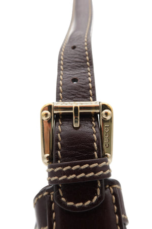 Close-up of a dark brown leather strap with beige contrast stitching and a gold-tone buckle. The buckle has 'GUCCI' engraved vertically on the side.