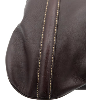 Close-up of a dark brown leather item, likely a handbag or leather accessory, showing the texture of the leather and a contrasting light beige stitching detail along a seam, set against a plain white background.