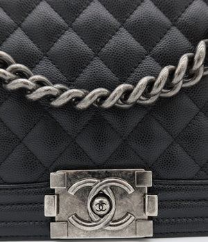 Close-up of a black quilted leather handbag with a silver-tone chain strap and a prominent interlocking CC turn-lock clasp, showing the Chanel logo.