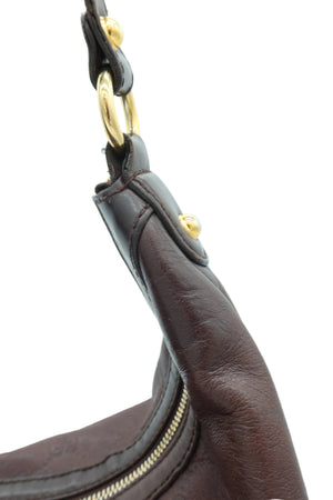 Close-up detail of a dark brown leather handbag showing the strap attachment with gold-tone hardware and a zipper.