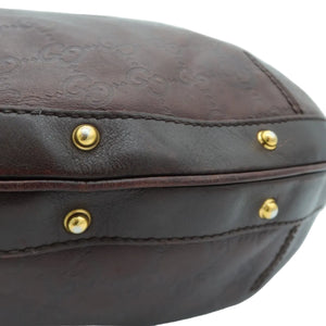 Close-up of a dark brown leather handbag showing the embossed Gucci monogram pattern, a stitched leather trim, and gold-tone metal rivets against a light gray background.