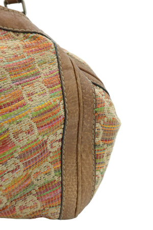 Close-up of a vintage woven handbag corner showing a multicolor striped patterned fabric and tan leather trim on a white background.