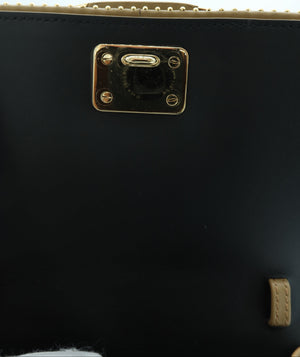 Close-up of a black leather handbag showing a gold-tone metal lock clasp and a light beige leather trim along the top edge.