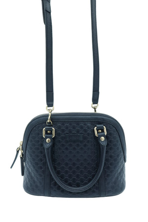 A black textured dome handbag with a top handle, a detachable shoulder strap, and gold-tone hardware, shown against a light blue studio background.
