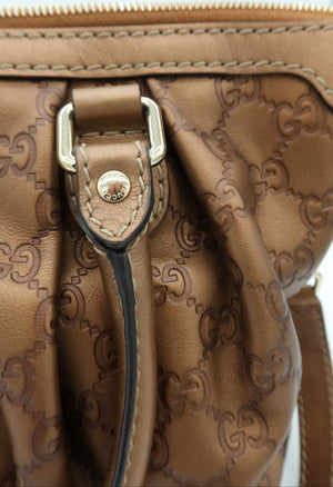 Close-up of a brown leather handbag with an embossed monogram pattern, a gold-tone metal buckle, and a black leather strap detail.