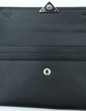 Close-up of a black textured leather or faux-leather accessory with a snap button closure and a triangular metal clasp on a white background.