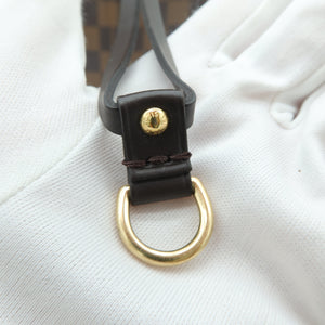 Close-up of a dark brown leather strap with a gold-tone D-ring and a small gold snap button, resting on a white textured surface with a brown checkered pattern visible in the background.
