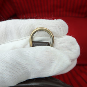 A close-up of a white cotton glove holding a gold-tone metal D-ring with a dark strap, set against a red striped Louis Vuitton bag interior.
