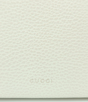 Close-up of a light cream pebbled leather surface with the embossed brand name GUCCI centered near the bottom.