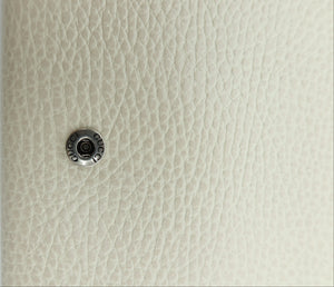 Close-up of a small round silver metal button or snap fastener attached to a textured off-white pebbled surface next to a plain white vertical edge.