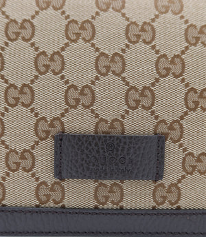 Close-up of a Gucci monogram canvas bag in beige and brown with a dark brown leather patch embossed with the Gucci logo.