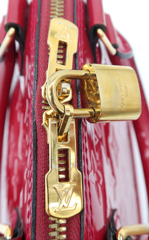 A close-up of a Louis Vuitton red patent leather bag featuring a gold-tone zipper, padlock, and hardware on a white background.