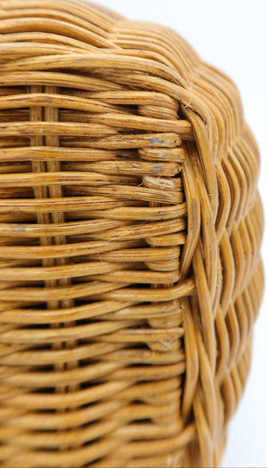Close-up of a light brown woven wicker basket corner showing the detailed texture of the interlaced strands against a white background.
