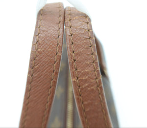 Close-up detail of a brown leather strap with fine stitching and a gold-toned zipper, attached to a light-colored bag against a white background.
