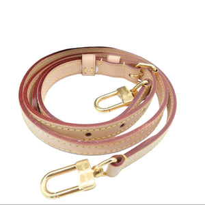A light beige leather shoulder strap with gold-tone hardware, displayed on a white surface next to a brown monogram bag.