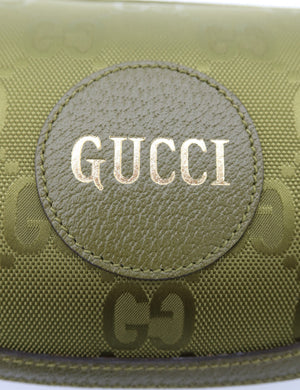 Close-up of a Gucci pouch in olive green GG Supreme canvas with a circular leather patch featuring the brand name 'GUCCI' in gold lettering.