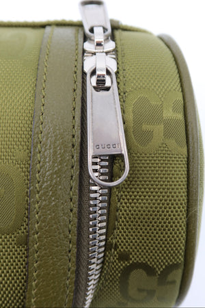 Close-up of an olive green Gucci zippered pouch featuring the brand's monogram pattern and a silver-tone metal zipper pull engraved with 'gucci'.