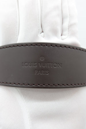 A close-up of a Louis Vuitton leather belt with 'LOUIS VUITTON PARIS' embossed on a white fabric background.
