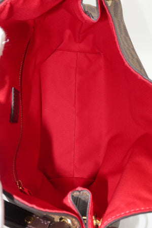 Close-up of the interior of a red handbag, showing the red fabric lining, zipper pocket, and a portion of the brown monogram canvas exterior.