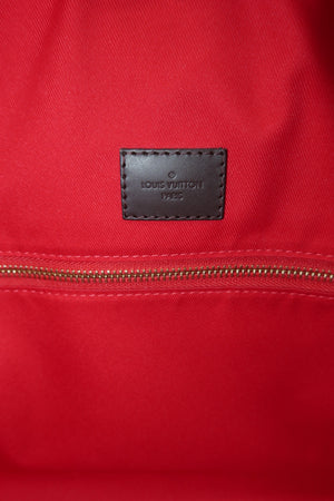 Close-up of a red Louis Vuitton fabric item with a brown leather logo patch reading Louis Vuitton 1947 and a gold zipper.