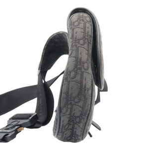 A close-up of a black shoulder bag with a textured, embossed monogram pattern, showing the strap and side profile against a white background.