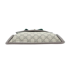 A Gucci clutch bag in beige GG Supreme canvas with brown leather trim and a green bow detail on the front, shown against a plain white background.