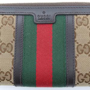 Gucci monogram canvas zip-around wallet with green and red web stripe and dark brown leather trim, featuring a central Gucci logo plaque.