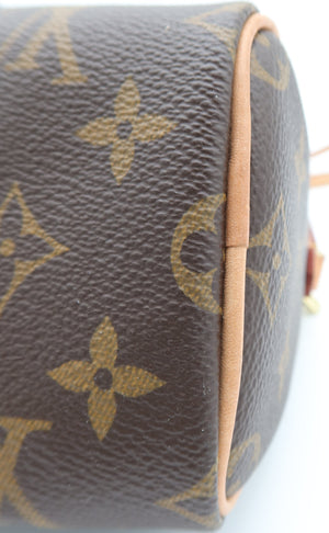 Close-up of a Louis Vuitton monogram canvas toiletry bag corner showing the brown coated canvas with tan monogram print and light tan leather trim on a white background.