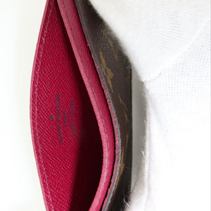 Close-up of an open Louis Vuitton wallet showing a bright magenta-pink interior lining and the brand name printed inside, next to a white textured fabric background.