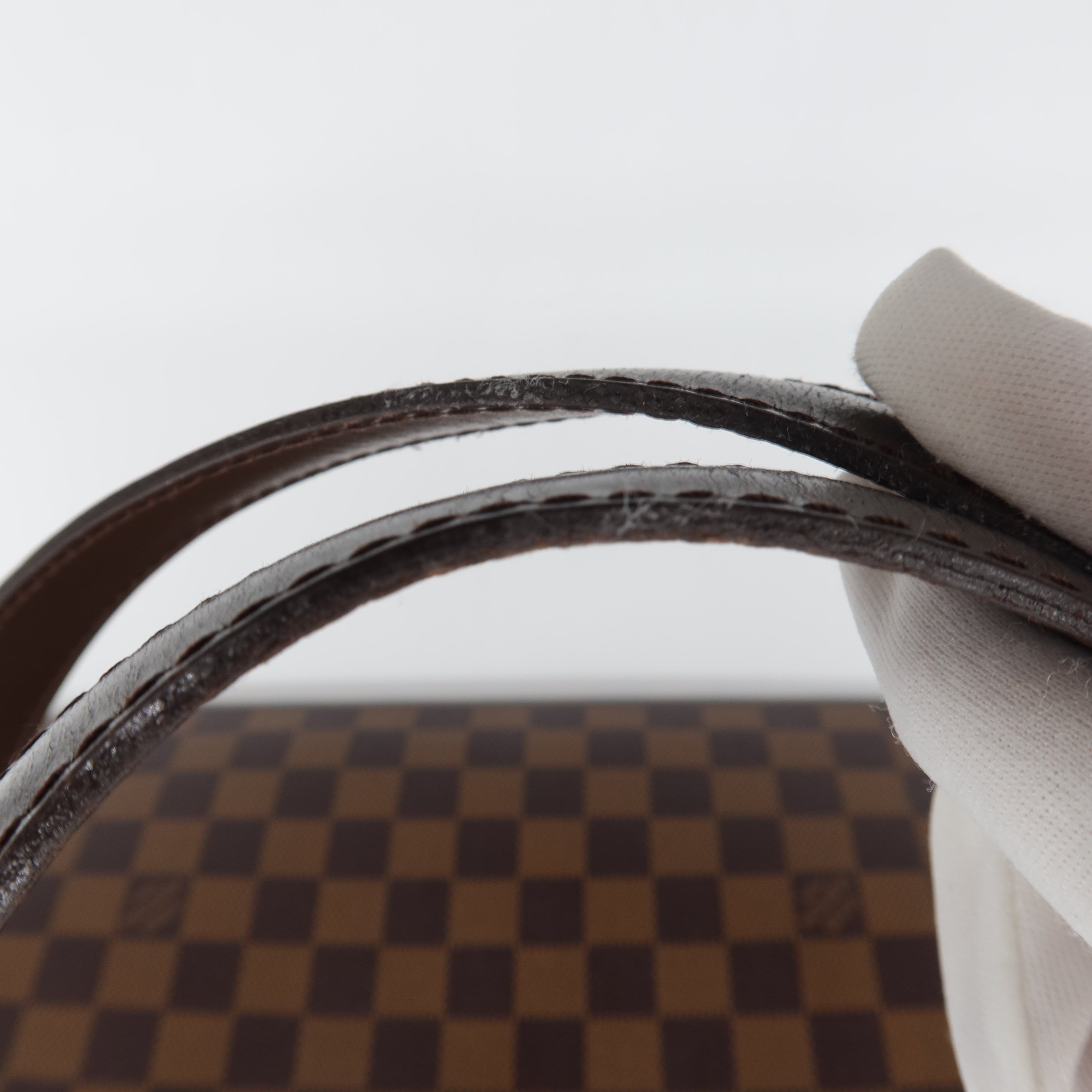 A close-up of a hand wearing a white glove holding a dark brown leather strap in front of a brown and beige checkered patterned background.