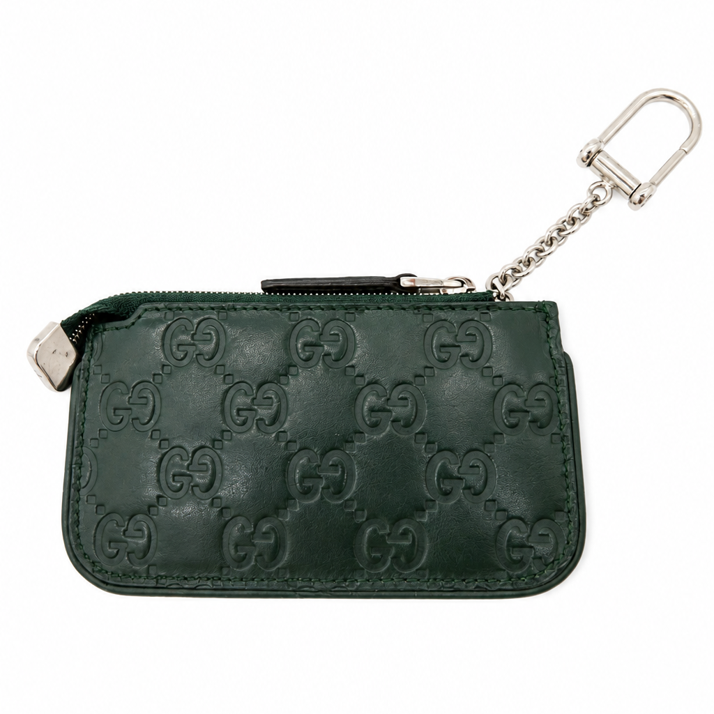 A dark green leather pouch featuring an embossed GG monogram pattern, with a silver-tone metal zipper pull and a matching interlocking GG chain keychain, shown against a plain white background.
