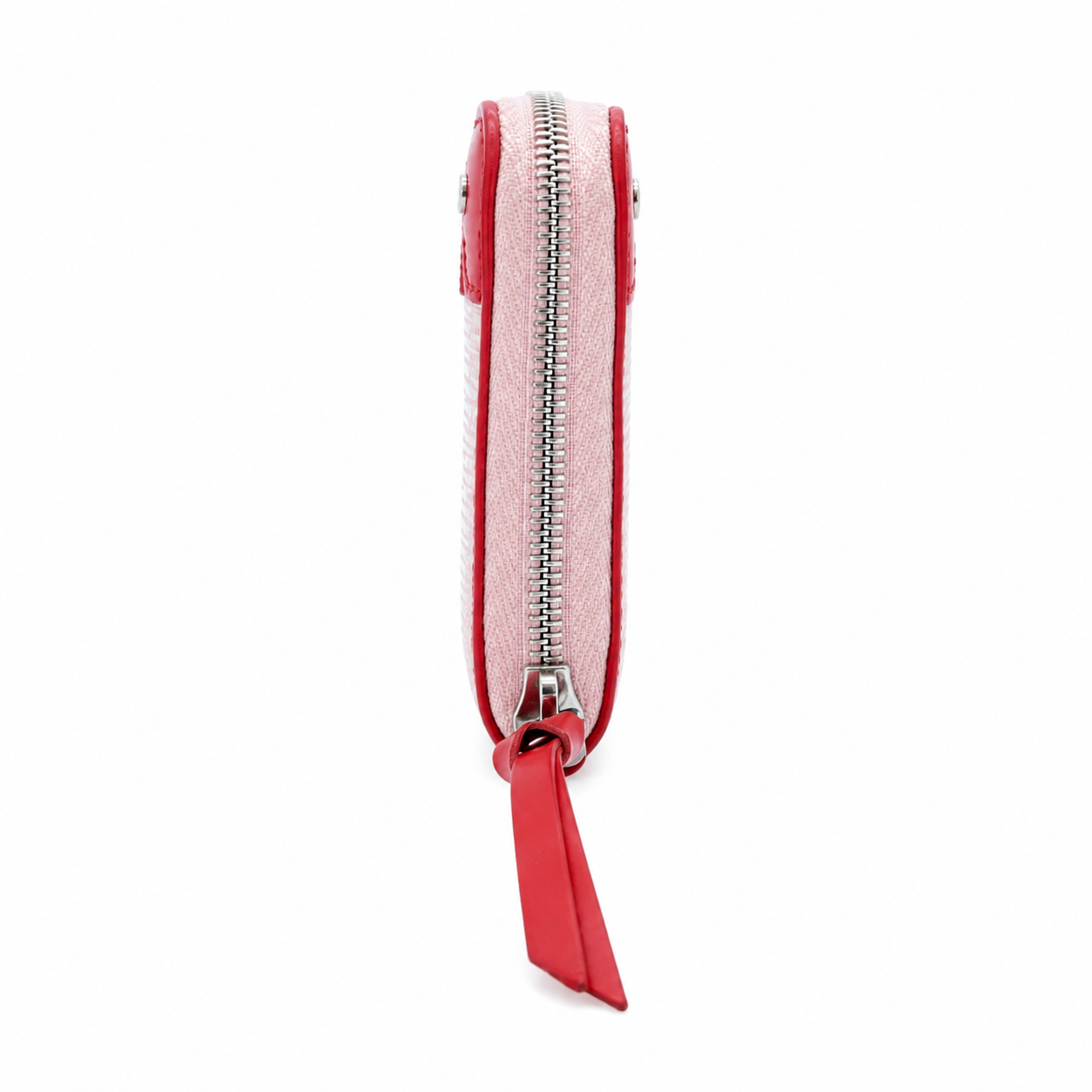 A slim zip-around pouch shown from the side on a plain white background. The pouch has a light pink woven or textured exterior with bright red trim and a matching red zipper pull tab.