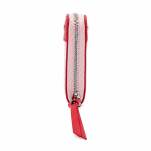 A slim zip-around pouch shown from the side on a plain white background. The pouch has a light pink woven or textured exterior with bright red trim and a matching red zipper pull tab.