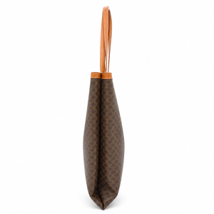 A brown coated canvas tote bag with a repeating monogram pattern and a light brown leather handle, shown from the side against a white background.