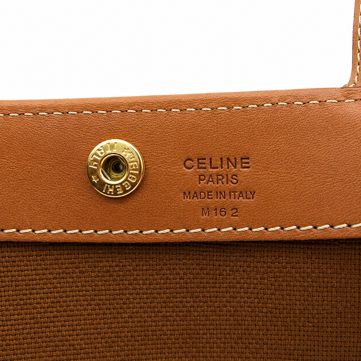 Close-up of a Celine shoulder bag showing a tan leather flap with a gold-tone snap button and embossed 'CELINE PARIS MADE IN ITALY M 16 2' text, alongside a brown canvas body.