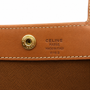 Close-up of a Celine shoulder bag showing a tan leather flap with a gold-tone snap button and embossed 'CELINE PARIS MADE IN ITALY M 16 2' text, alongside a brown canvas body.