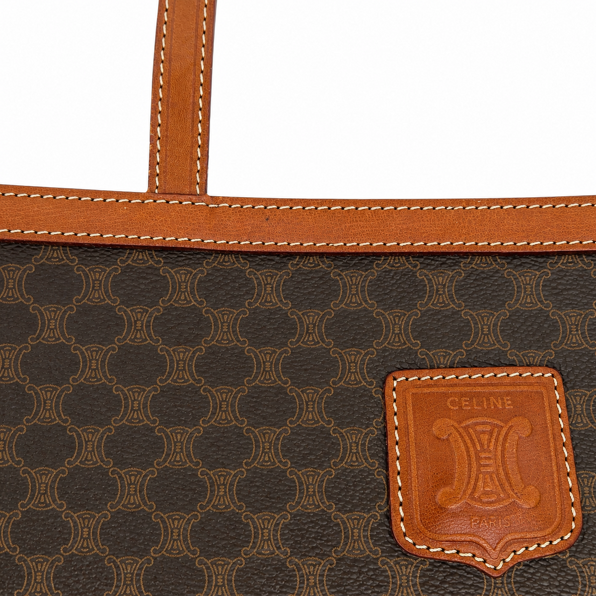 Close-up of a Celine handbag featuring dark brown coated canvas with the signature repeating CC monogram and tan leather trim, including a leather patch with the Celine logo.